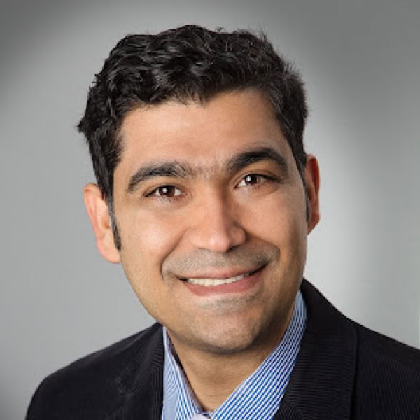 Man with facial hair sitting indoors using smartphone, focusing on screen.